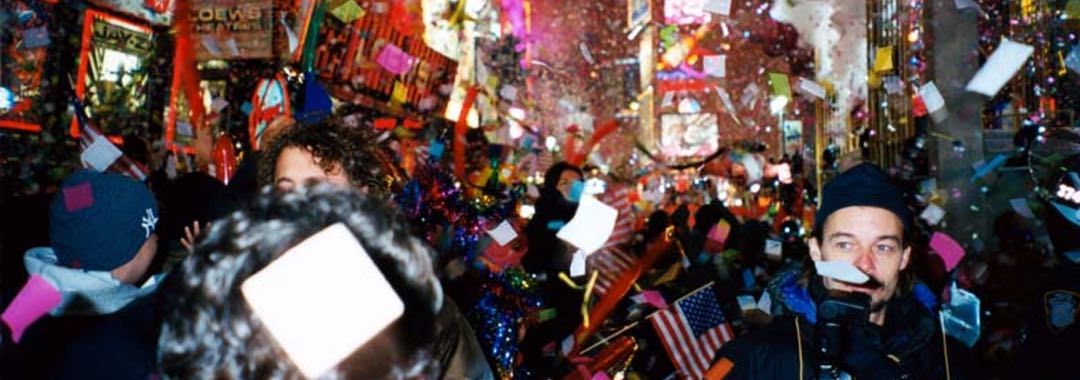 Nighttime photo of a crowd of people celebrating in Times Square in New York with confetti falling and bright lights